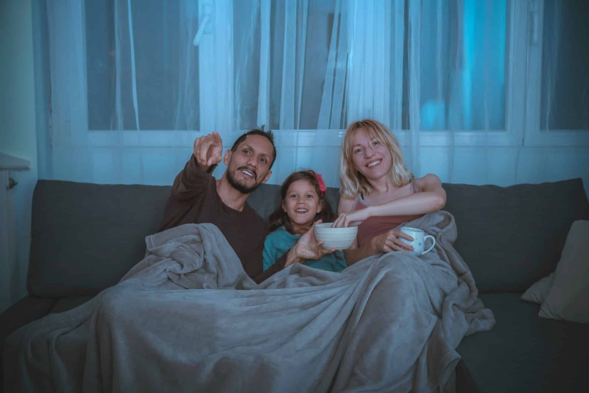 G-Rated Movies - A family watching a movie and eating popcorn in the furniture at home.